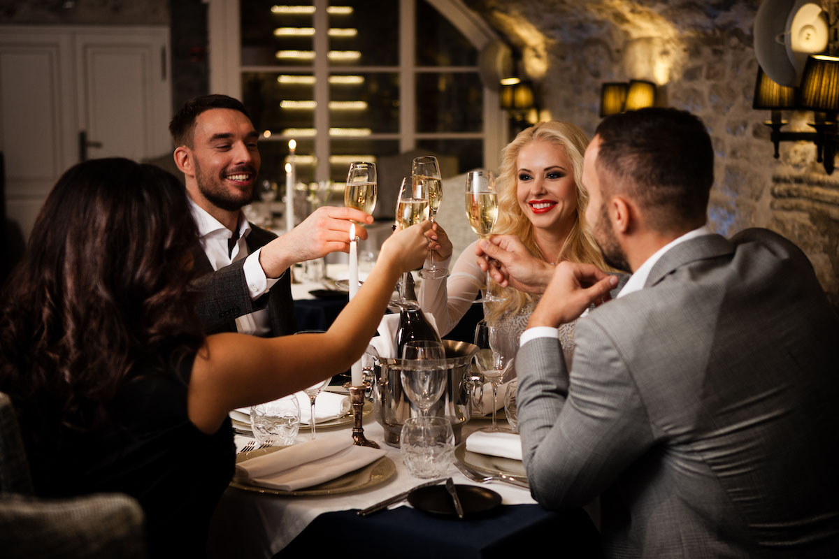 four friends at a formal dinner table cheers champagne