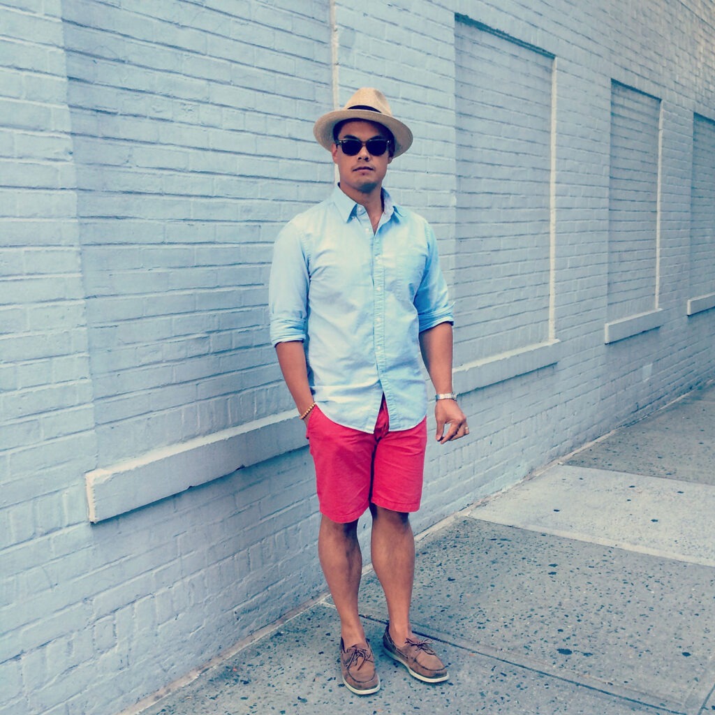 man wearing blue oxford shirt with red shorts and panama hat