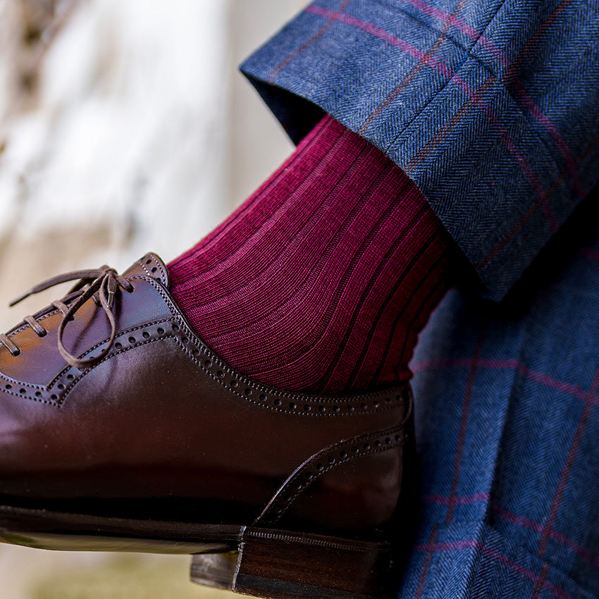 man crossing legs wearing burgundy wool dress socks with navy windowpane trousers and dark brown dress shoes