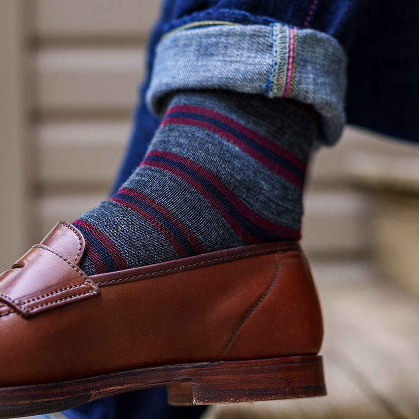 man crossing ankles wearing striped grey dress socks with jeans and penny loafers