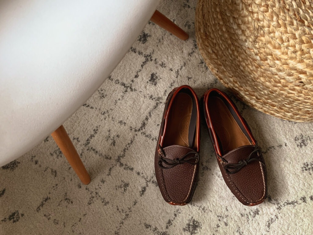 close up of llbean bison leather slippers on a light rug next to an ottoman and chair