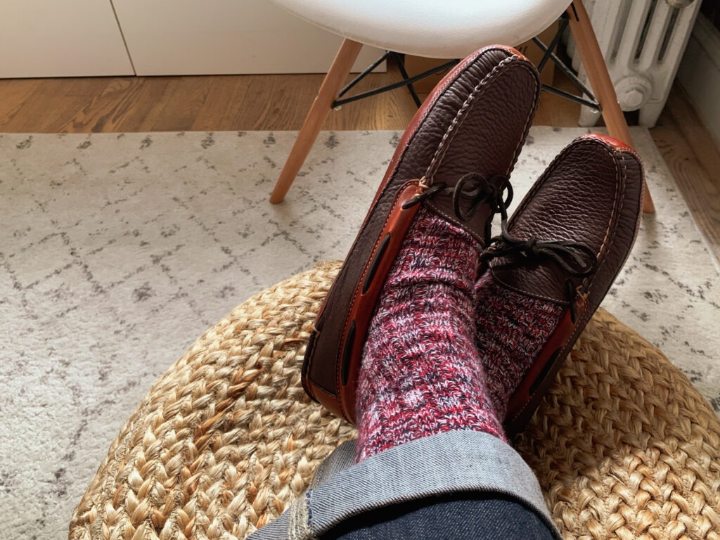 close up of man feet wearing burgundy wool socks with brown leather slippers in living room