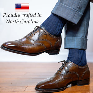 man crossing legs wearing navy wool dress socks with a grey windowpane suit and brown oxfords