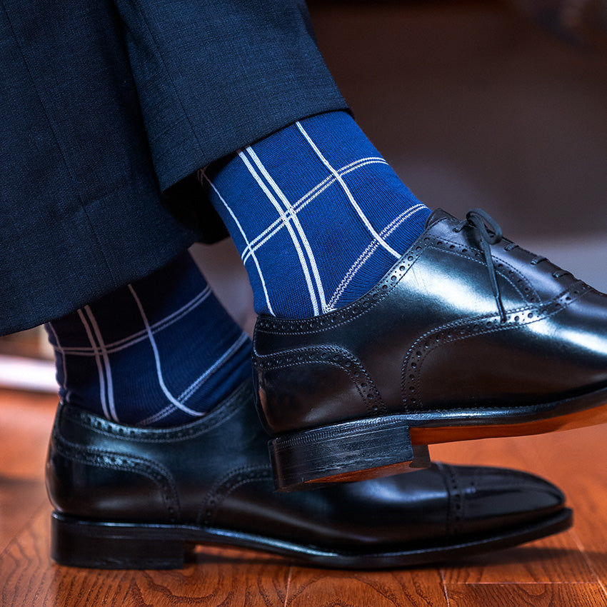 man crossing ankles wearing navy blue windowpane dress socks with black oxfords and navy slacks